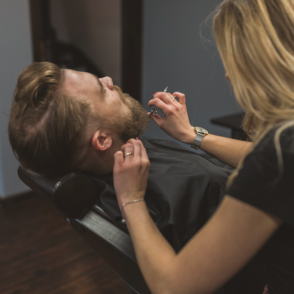 Barber trimming man's beard.